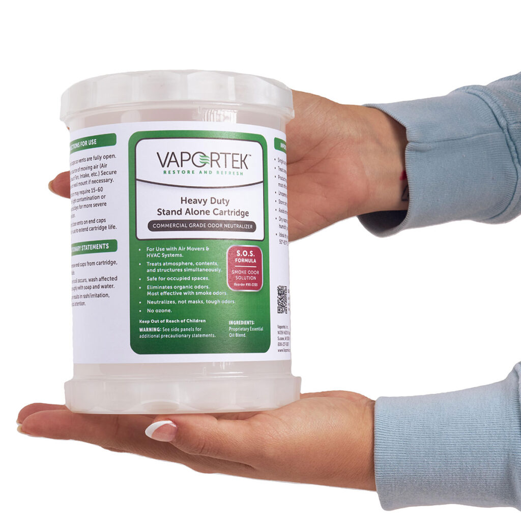 A person in a blue long-sleeve shirt holds a large white container labeled Heavy-Duty Stand Alone Cartridge 2.0, designed for commercial grade odor neutralization.