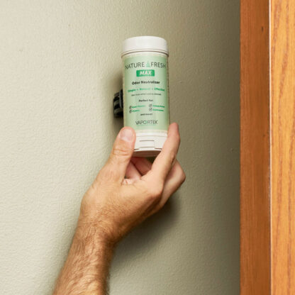 A person mounts a Fresh & EZ Combo Kit odor neutralizer canister, featuring white and green colors, on a beige wall next to a wooden door frame.